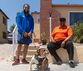 Photo of two men and a dog on the steps in front of a house