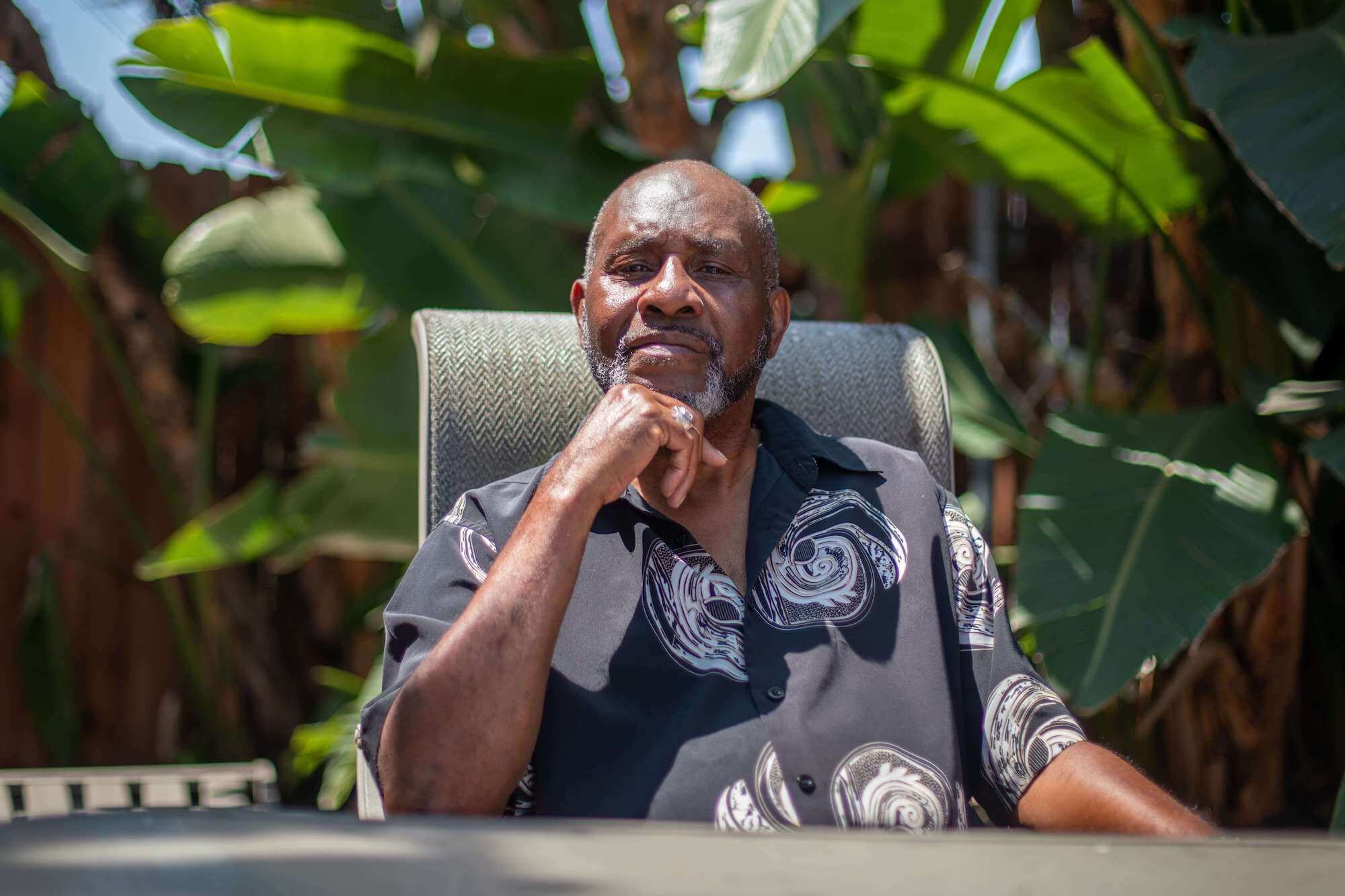 Seated man in front of lush green foliage